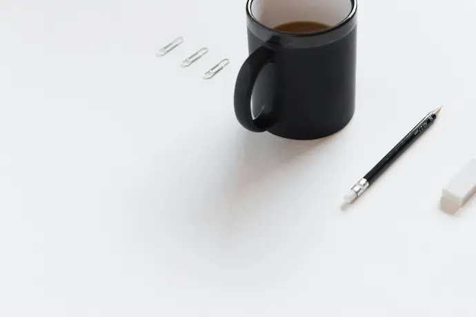 three white paper clips, black ceramic mug, black pencil, and white pencil eraser on white surface